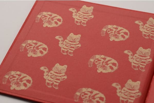 表紙を開くと赤い見返し部分にたくさんの金のスタンプ風印刷のとらねこが！　(c)JIROCHO, Inc. / KODANSHA